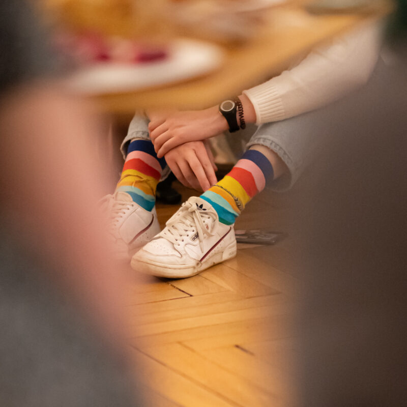 Chaussettes arc-en-ciel et baskets blanches, intérieur parqueté.