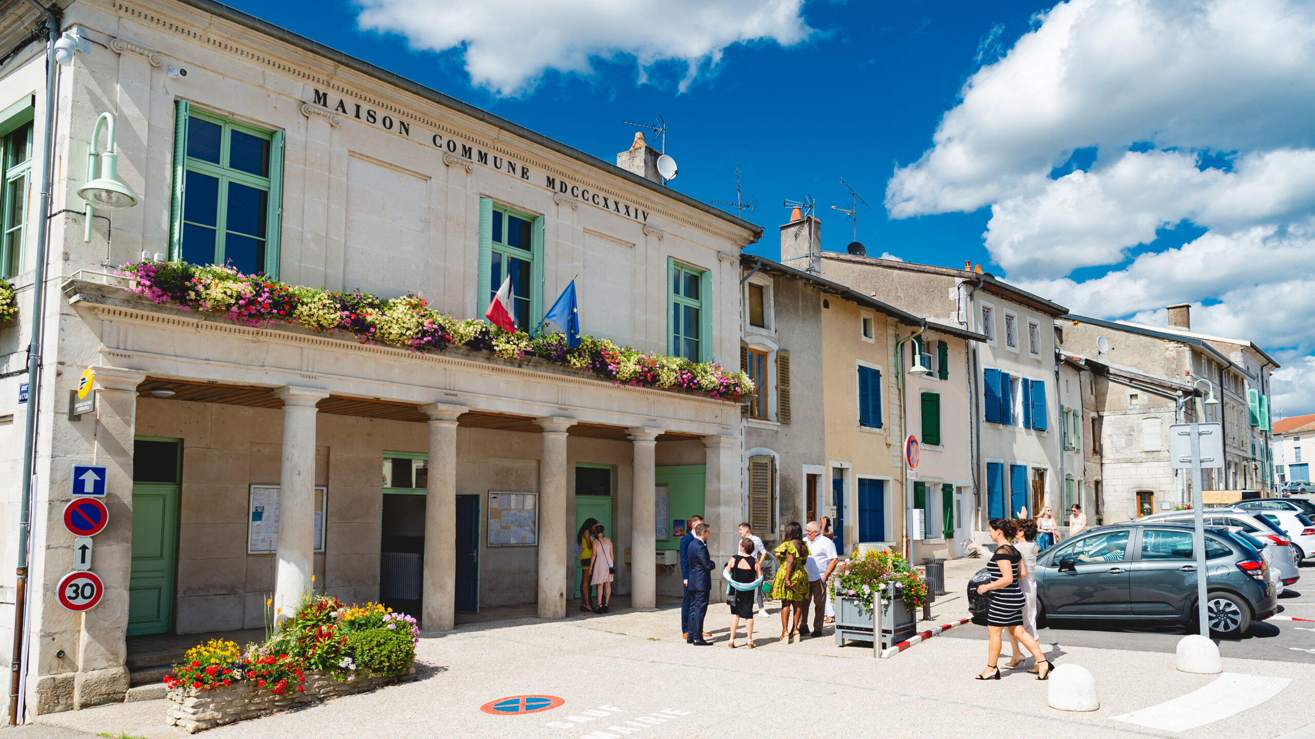 Mairie avec fleurs et personnes devant.