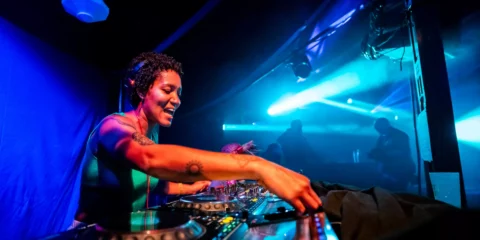 DJ femme souriante mixant sur des platines en discothèque.