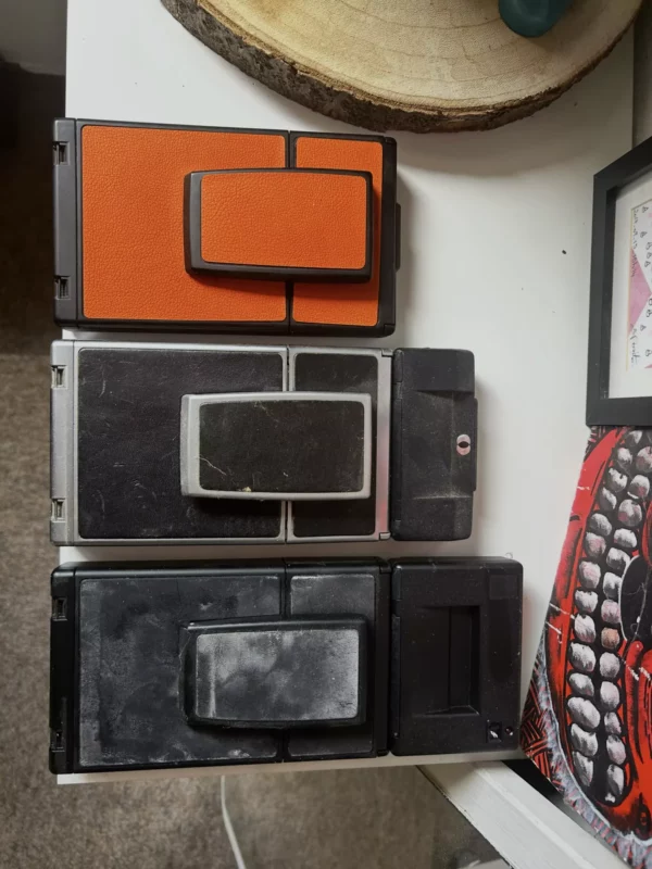 Trois appareils photo instantanés pliables vintage alignés verticalement.