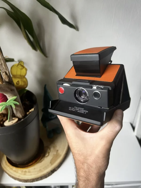 Main tenant un appareil photo Polaroid SX-70 vintage noir et orange.