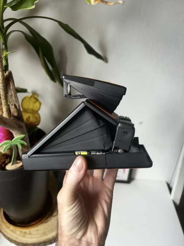 Appareil photo Polaroid SX-70 vintage tenu par une main.