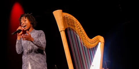 Chanteuse sur scène avec microphone et grande harpe en bois.