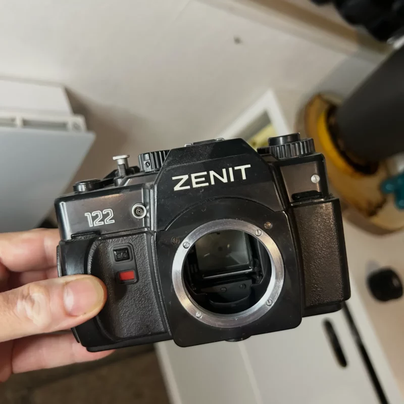 Appareil photo argentique Zenit 122 tenu par une main.