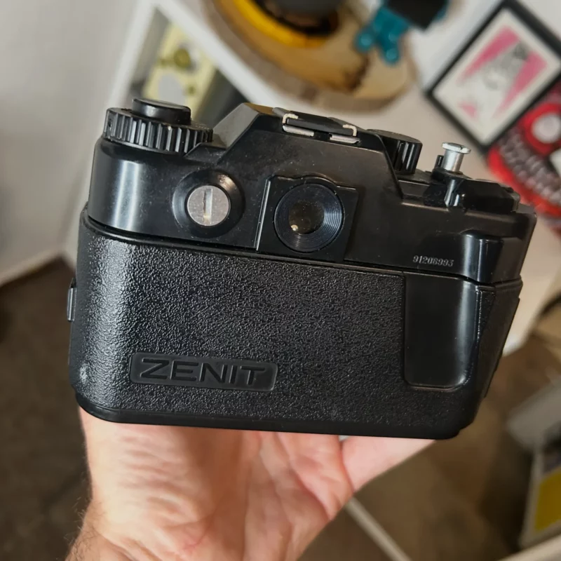 Appareil photo argentique Zenit noir tenu à la main.