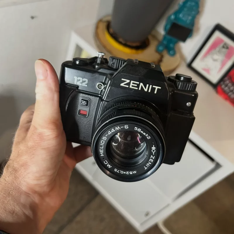 Appareil photo argentique Zenit 122 tenu à la main.