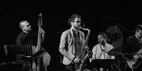 Quartet de jazz en concert sur une scène sombre.