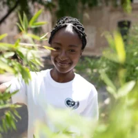 Femme souriante en t-shirt blanc parmi des feuilles vertes.