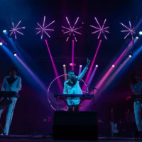 Chanteur en blanc sur scène sous des néons roses.