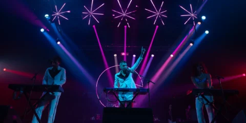 Chanteur en blanc sur scène sous des néons roses.