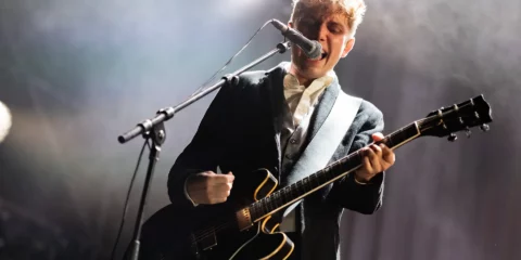 Chanteur guitariste sur scène sous des projecteurs brillants.
