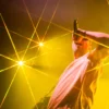 Chanteur sur scène entouré de faisceaux lumineux jaunes.