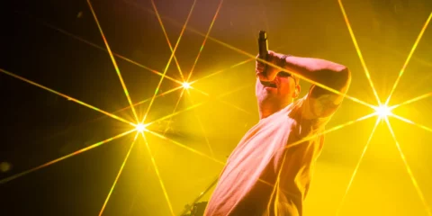 Chanteur sur scène entouré de faisceaux lumineux jaunes.